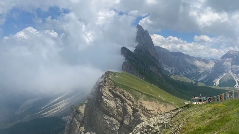 Vista panoramica su una cima dolomitica tra le nuvole, con alcuni escursionisti su un punto panoramico